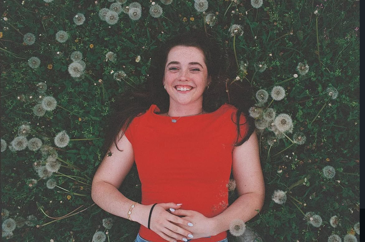 Desiree lying in a field of dandelions wearing a red top